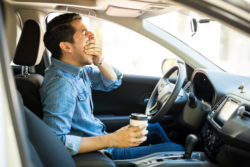 Young man feeling tired and yawning while driving a car